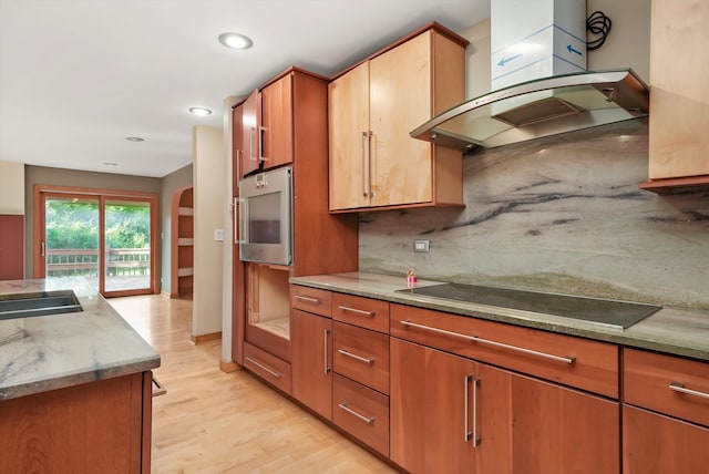 kitchen with decorative backsplash, light wood-type flooring, light stone counters, black electric cooktop, and wall chimney range hood