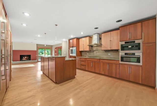 kitchen with a center island, light hardwood / wood-style floors, wall chimney range hood, and hanging light fixtures