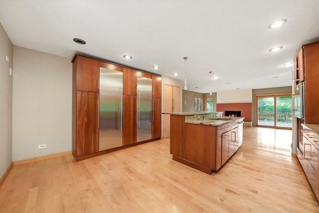 kitchen with light stone countertops, pendant lighting, light wood-type flooring, a center island with sink, and appliances with stainless steel finishes