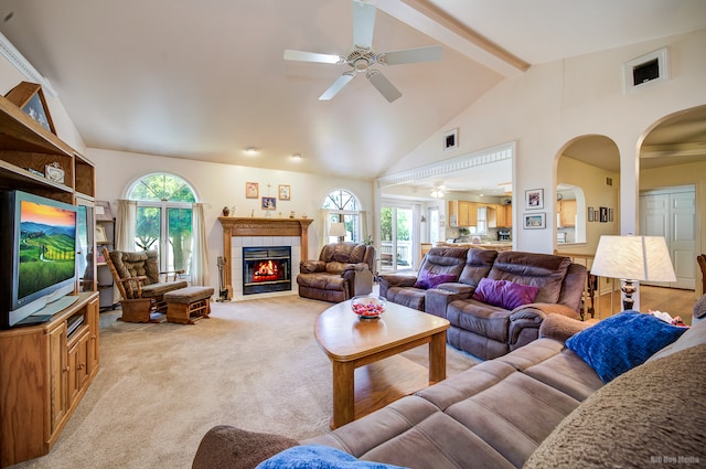 carpeted living room with a tile fireplace, ceiling fan, beamed ceiling, and high vaulted ceiling