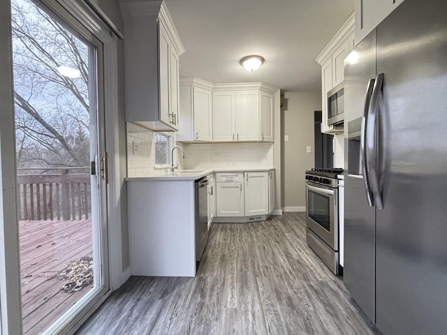 kitchen featuring white cabinetry, sink, stainless steel appliances, backsplash, and hardwood / wood-style flooring