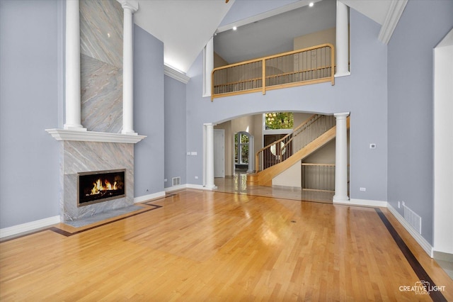 unfurnished living room with a high end fireplace, a high ceiling, ornate columns, and wood-type flooring