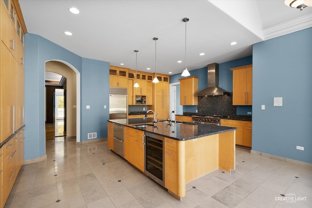 kitchen with sink, hanging light fixtures, beverage cooler, wall chimney range hood, and an island with sink