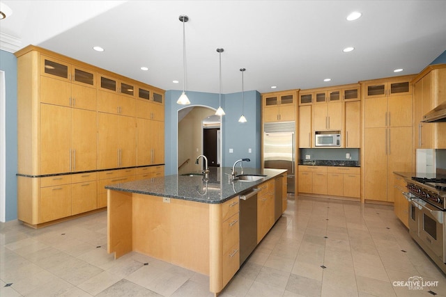 kitchen featuring pendant lighting, sink, built in appliances, dark stone countertops, and a large island