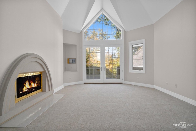 unfurnished living room featuring light colored carpet, high vaulted ceiling, and french doors