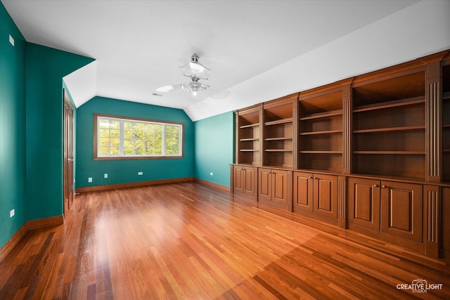 unfurnished living room with ceiling fan, wood-type flooring, lofted ceiling, and built in shelves