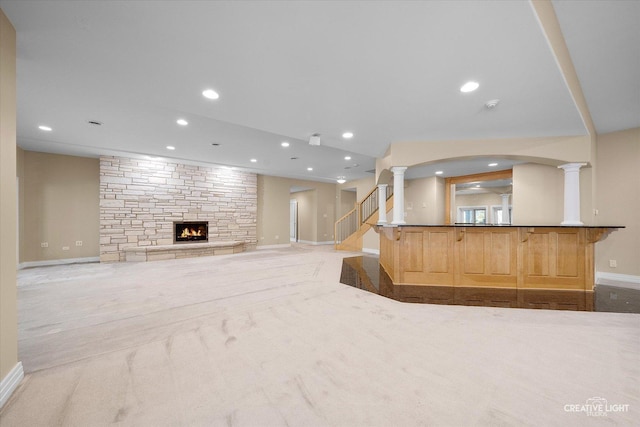 unfurnished living room featuring light carpet, decorative columns, and a stone fireplace