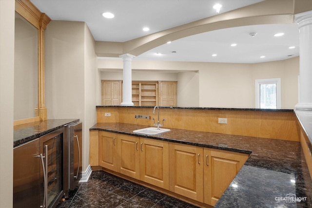 kitchen featuring kitchen peninsula, ornate columns, dark stone counters, sink, and wine cooler