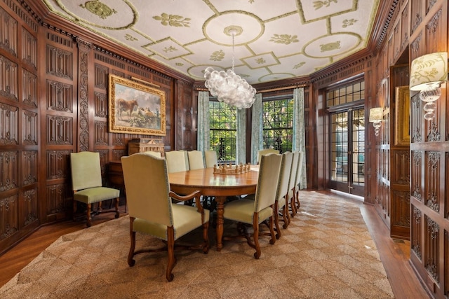 dining space featuring wooden walls, light hardwood / wood-style floors, a notable chandelier, and ornamental molding