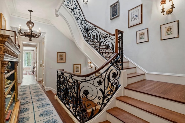 stairs with a notable chandelier, wood-type flooring, and ornamental molding