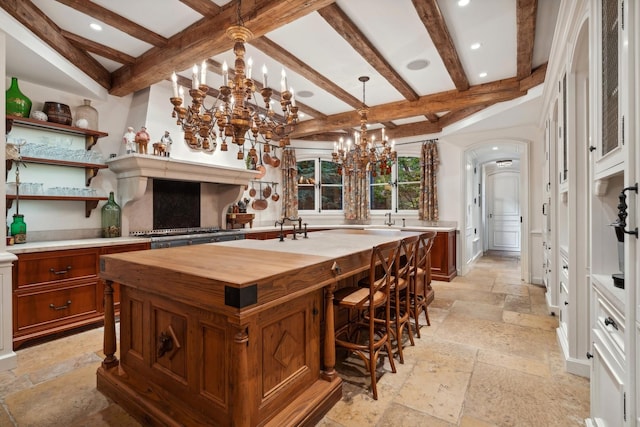 kitchen featuring beam ceiling, decorative light fixtures, a notable chandelier, and an island with sink