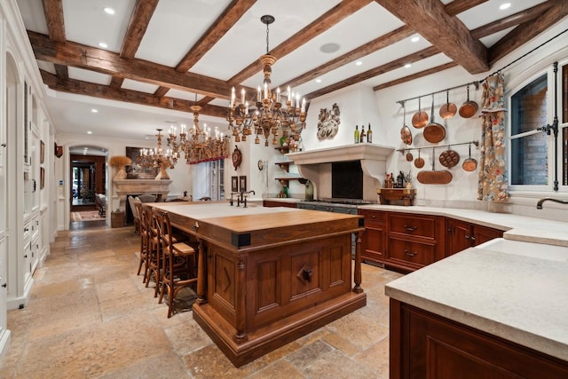 kitchen with sink, beam ceiling, pendant lighting, a center island with sink, and a chandelier