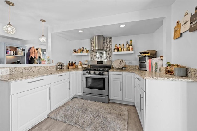 kitchen featuring kitchen peninsula, wall chimney exhaust hood, decorative light fixtures, white cabinetry, and stainless steel range with gas stovetop