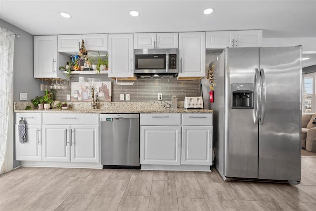 kitchen featuring backsplash, light stone countertops, white cabinetry, and stainless steel appliances