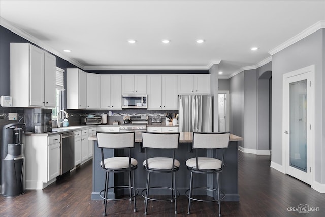 kitchen with white cabinets, dark hardwood / wood-style flooring, a kitchen island, and appliances with stainless steel finishes