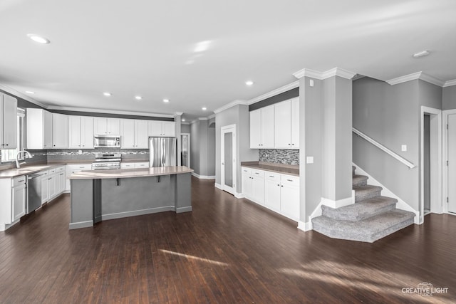 kitchen with appliances with stainless steel finishes, white cabinetry, a kitchen island, and dark wood-type flooring