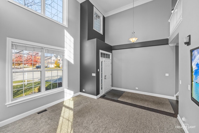 carpeted foyer entrance with a high ceiling, a wealth of natural light, and ornamental molding