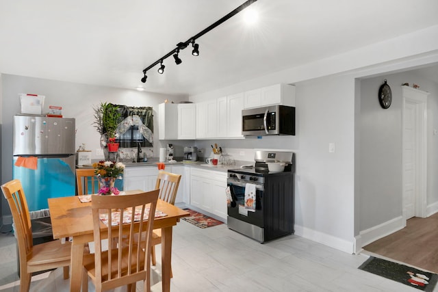 kitchen with white cabinets, sink, rail lighting, light hardwood / wood-style flooring, and stainless steel appliances