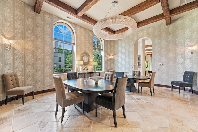 dining room featuring stone tile floors, baseboards, wallpapered walls, beam ceiling, and arched walkways