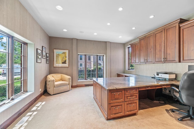 home office with a wealth of natural light, built in desk, and light colored carpet