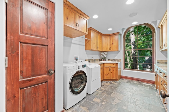 clothes washing area featuring stone finish floor, a sink, cabinet space, separate washer and dryer, and baseboards