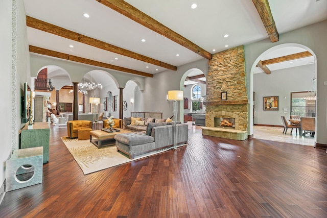 living room with a stone fireplace, wood finished floors, arched walkways, and a chandelier