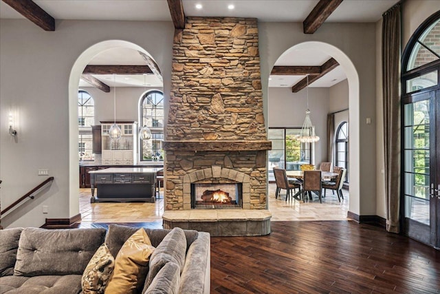 living area with beamed ceiling, wood finished floors, arched walkways, and baseboards