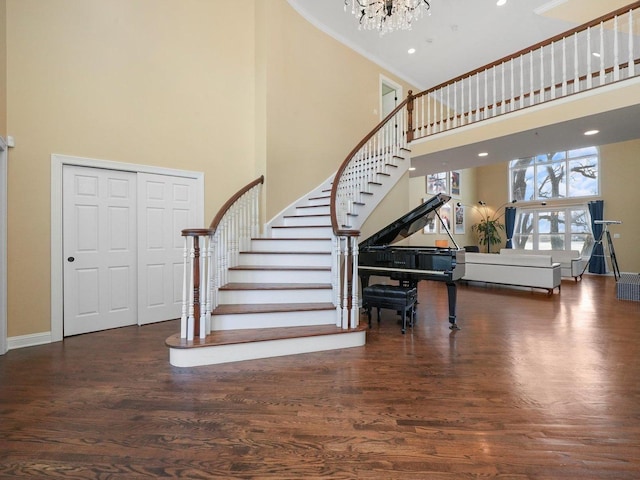 entryway with dark hardwood / wood-style flooring, a towering ceiling, crown molding, and an inviting chandelier