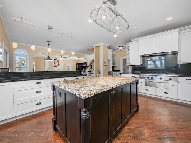 kitchen with backsplash, dark stone countertops, decorative light fixtures, a kitchen island, and ornamental molding