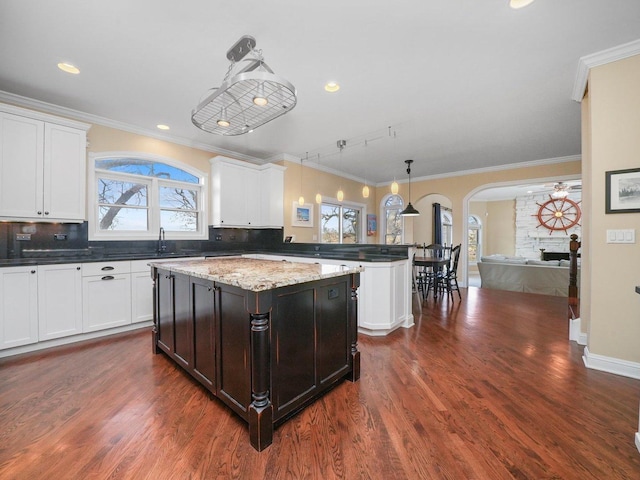 kitchen featuring light stone countertops, backsplash, a wealth of natural light, a fireplace, and hanging light fixtures