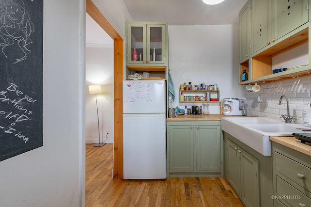 kitchen with backsplash, light hardwood / wood-style flooring, green cabinetry, and white refrigerator