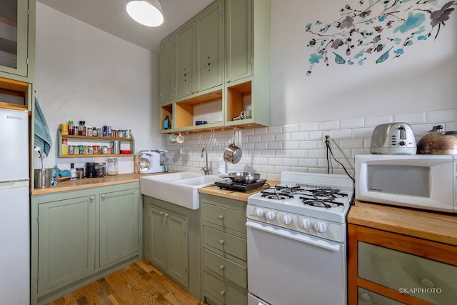 kitchen with white appliances, sink, green cabinetry, decorative backsplash, and light wood-type flooring