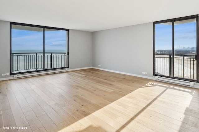 unfurnished room with a wall of windows, light hardwood / wood-style flooring, a water view, and a baseboard heating unit