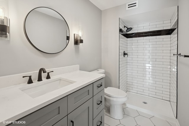 bathroom with a tile shower, tile patterned floors, vanity, and toilet