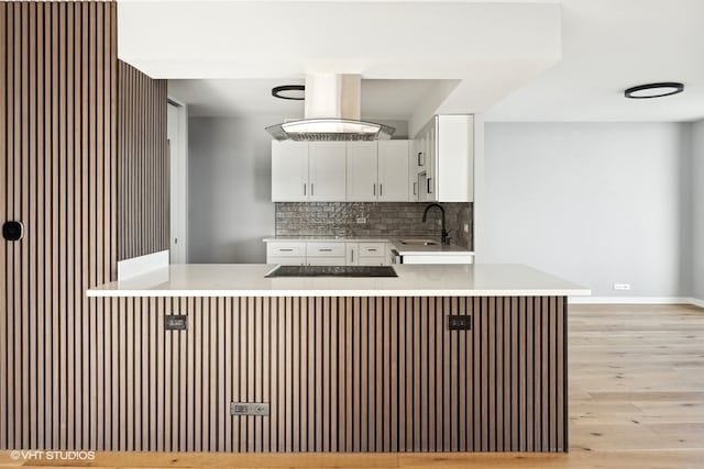 kitchen featuring backsplash, kitchen peninsula, sink, light hardwood / wood-style floors, and white cabinetry