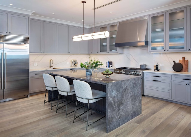 kitchen featuring dark stone counters, premium appliances, wall chimney range hood, pendant lighting, and a kitchen island