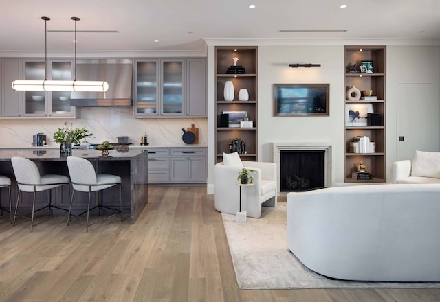 living room featuring light hardwood / wood-style floors, built in features, and crown molding