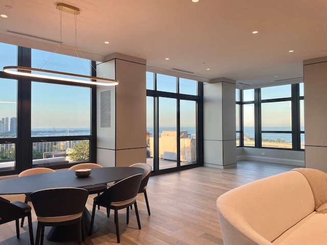 dining room featuring a water view, a wall of windows, and light hardwood / wood-style flooring