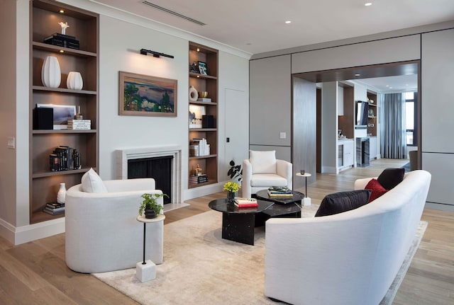 living room featuring built in features, crown molding, and light hardwood / wood-style flooring