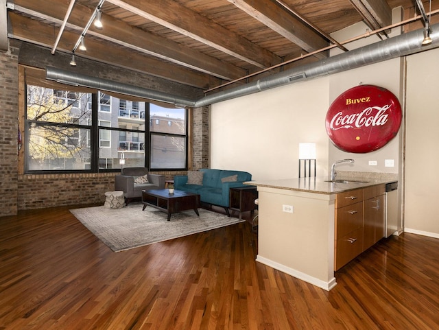 unfurnished living room featuring sink, rail lighting, dark hardwood / wood-style flooring, beamed ceiling, and brick wall