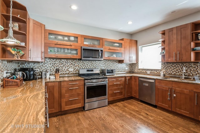 kitchen featuring light stone countertops, sink, backsplash, appliances with stainless steel finishes, and hardwood / wood-style flooring