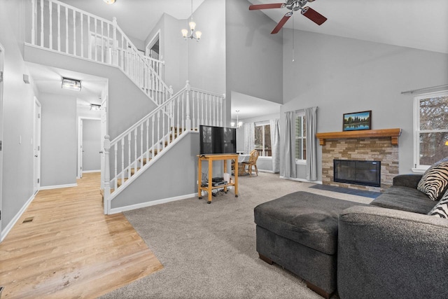 living room with ceiling fan with notable chandelier, carpet floors, high vaulted ceiling, and a stone fireplace