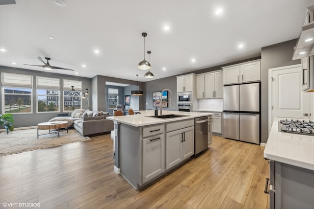 kitchen featuring ceiling fan, light wood-type flooring, stainless steel appliances, and a kitchen island with sink