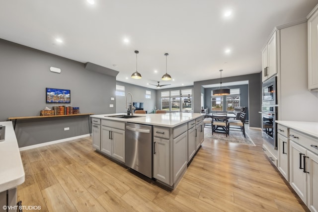 kitchen featuring stainless steel appliances, sink, decorative light fixtures, light hardwood / wood-style flooring, and a center island with sink