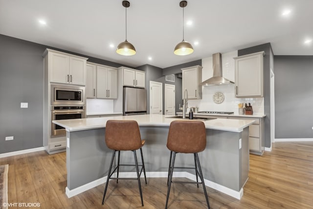 kitchen featuring pendant lighting, wall chimney exhaust hood, an island with sink, white cabinetry, and stainless steel appliances