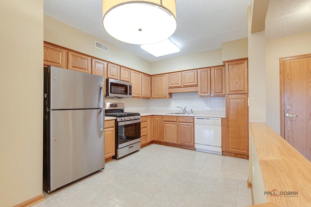 kitchen featuring decorative backsplash, a textured ceiling, stainless steel appliances, and sink