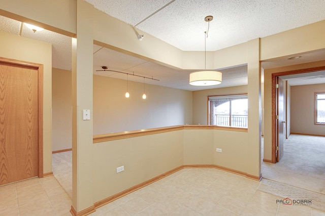 carpeted spare room featuring a textured ceiling, track lighting, and plenty of natural light