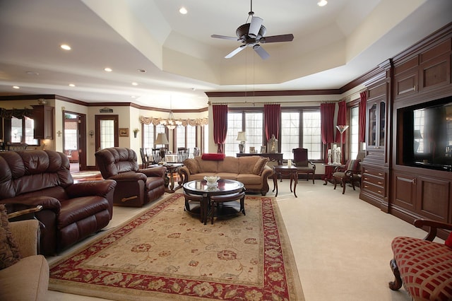 living room with light colored carpet, ceiling fan with notable chandelier, a raised ceiling, and ornamental molding