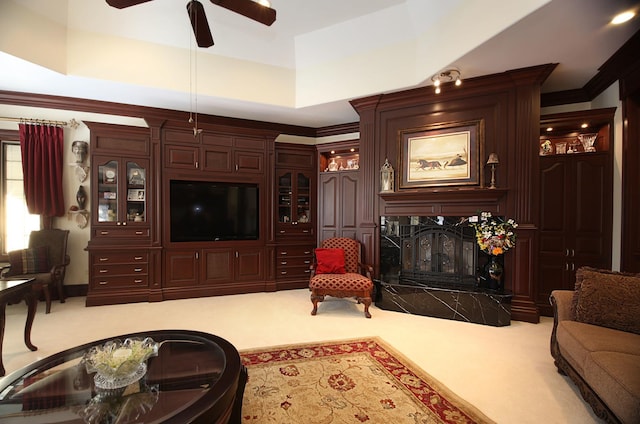 living room with ceiling fan, a raised ceiling, a high end fireplace, crown molding, and light carpet