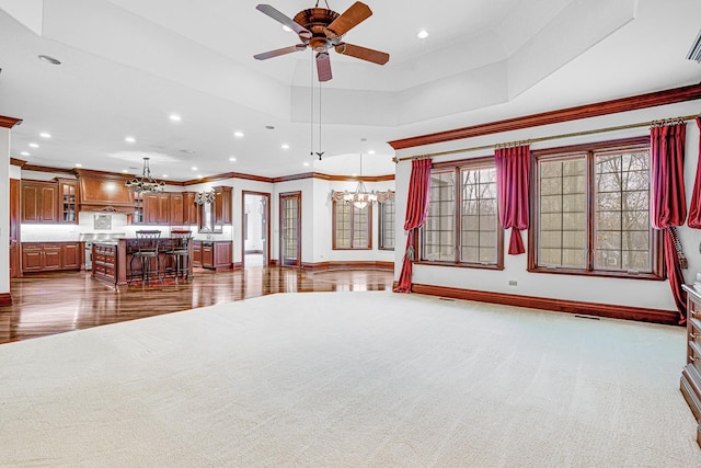 unfurnished living room featuring ceiling fan with notable chandelier, a raised ceiling, carpet floors, and ornamental molding